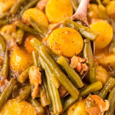 Serving spoon full of smothered green beans with potatoes.