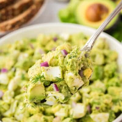 Avocado egg salad in white bowl with spoon.