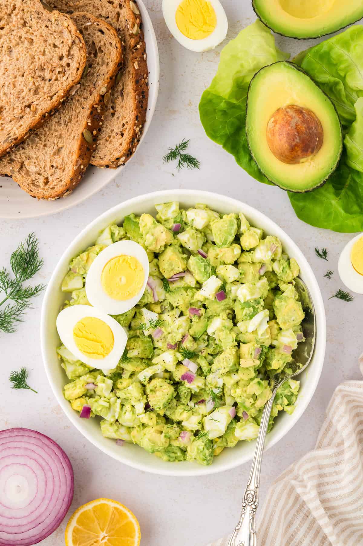 Avocado egg salad in white bowl with wheat bread.