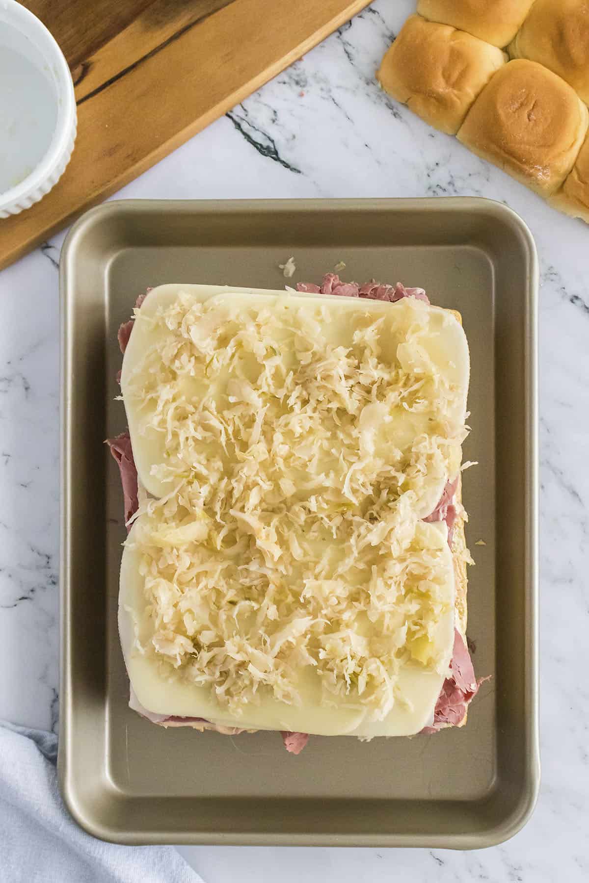 Ingredients layered on sandwich rolls to make reuben sliders.