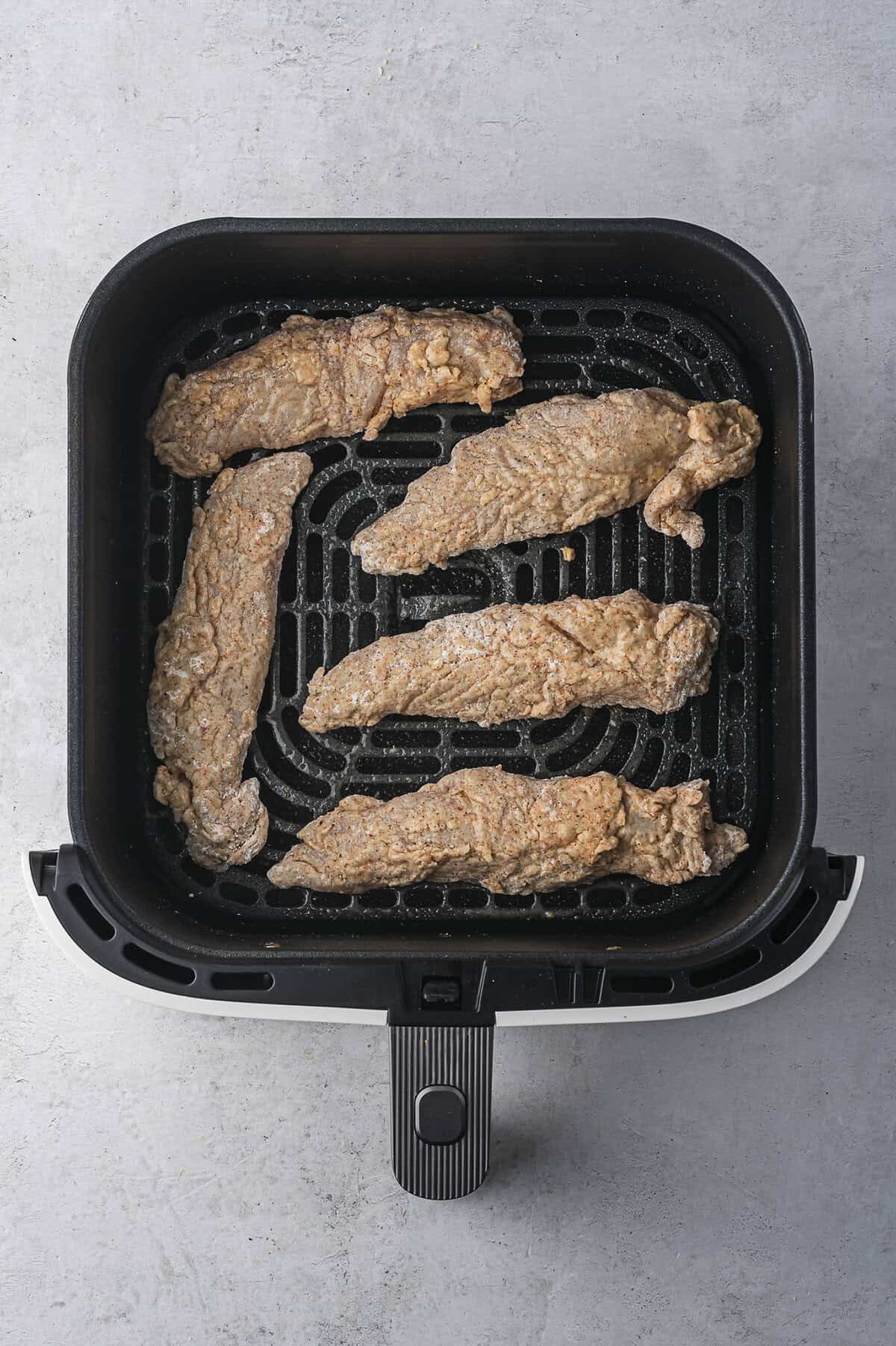 Chicken tenders in air fryer basket.