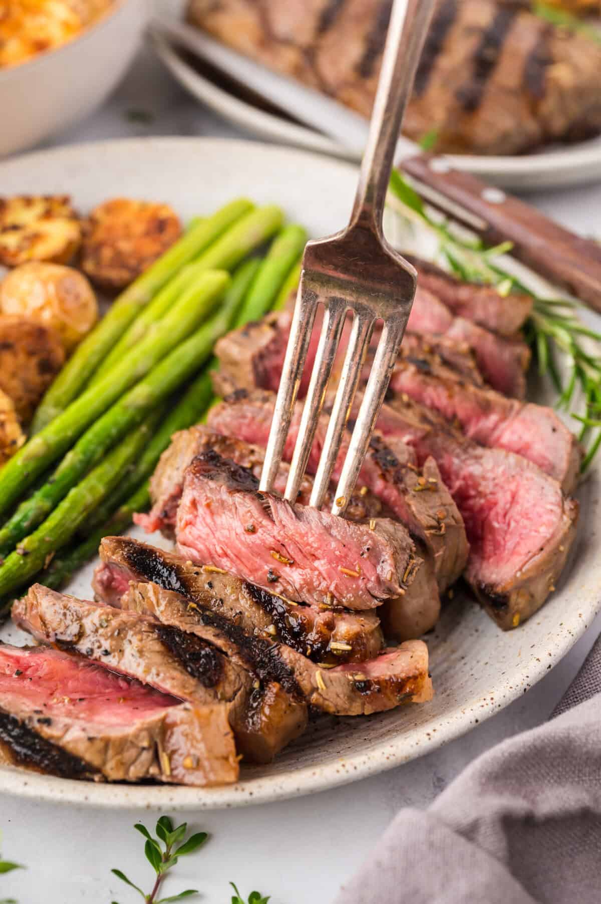 Medium rare steak sliced on plate next to asparagus and potatoes.