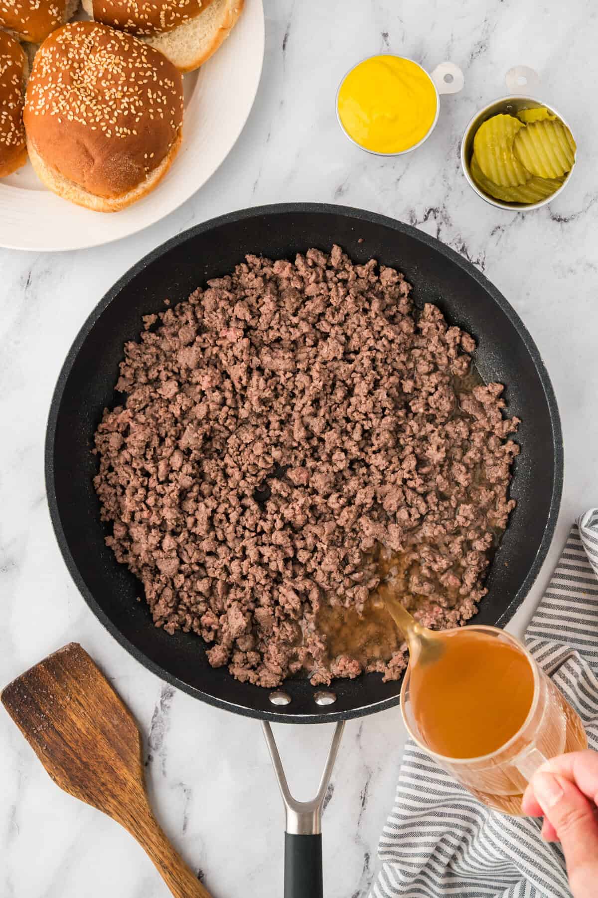 Beef broth being poured over ground beef.