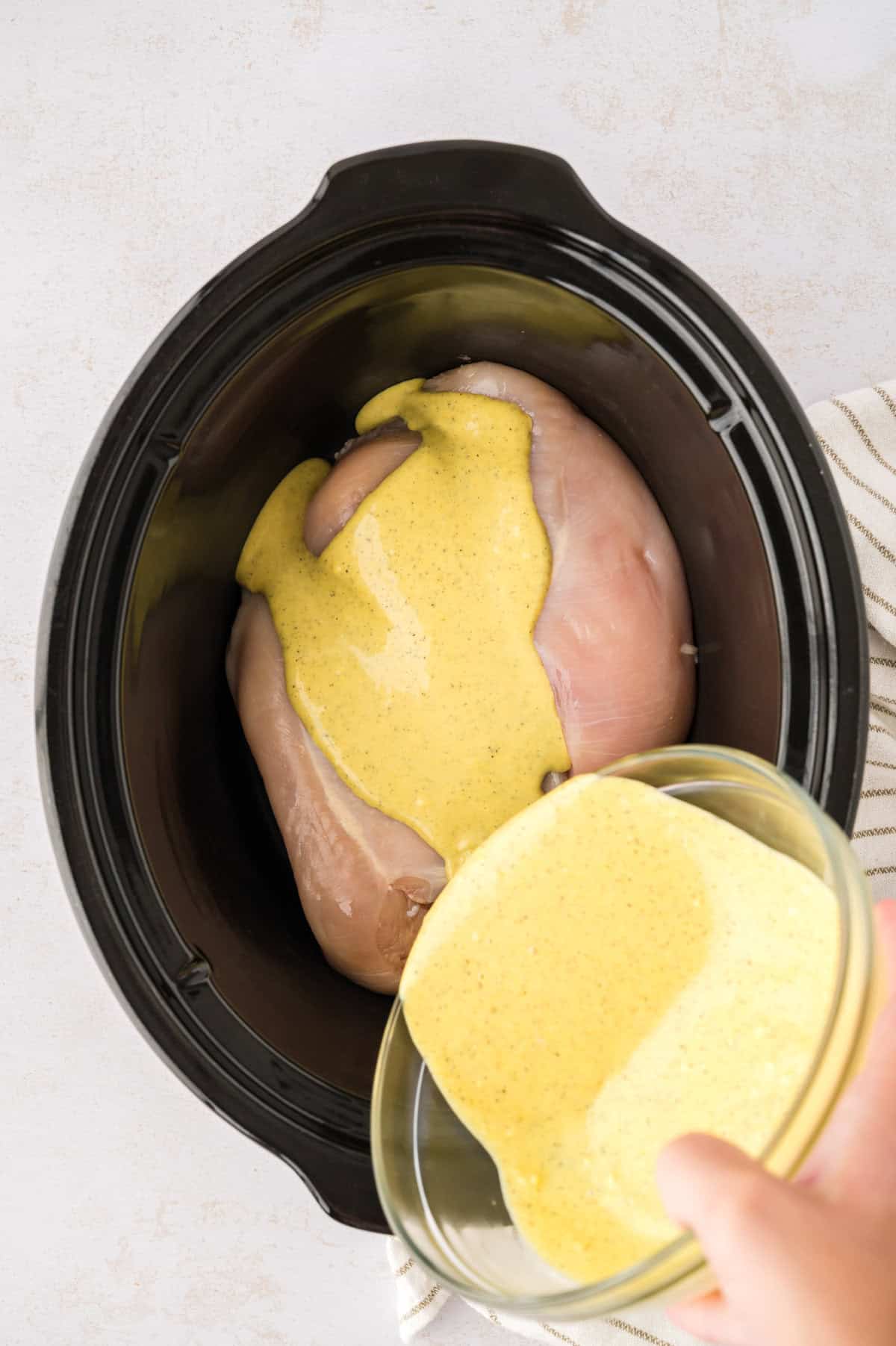 Honey mustard being poured over chicken breasts in crockpot.