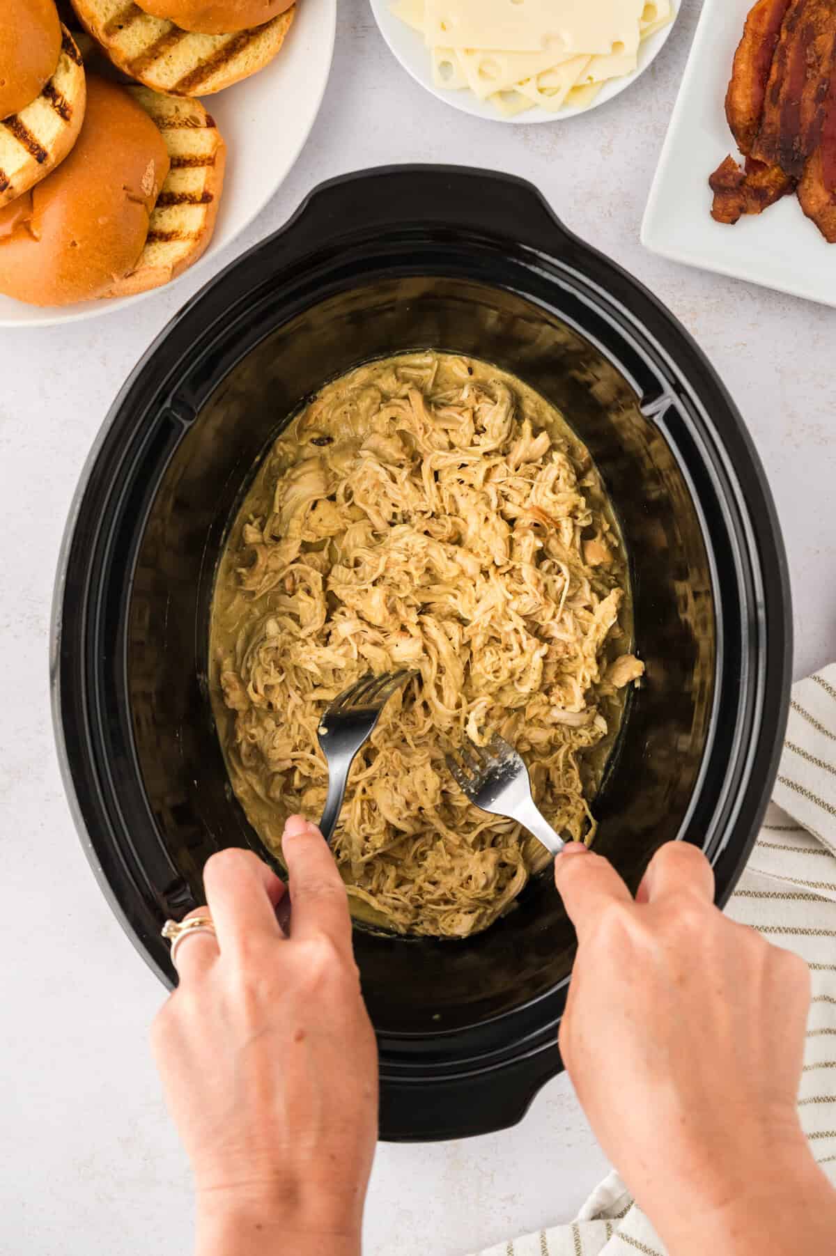 A person using two forks to shred honey mustard chicken in a crockpot.