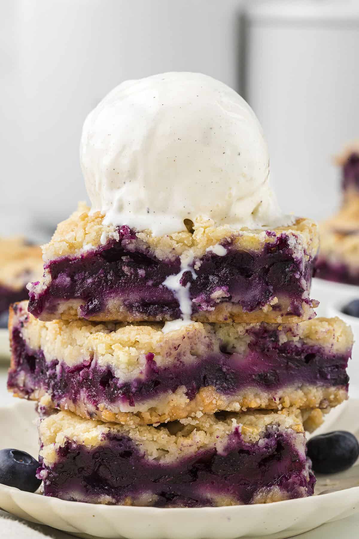 Blueberry pie bars topped with a scoop of vanilla ice cream.
