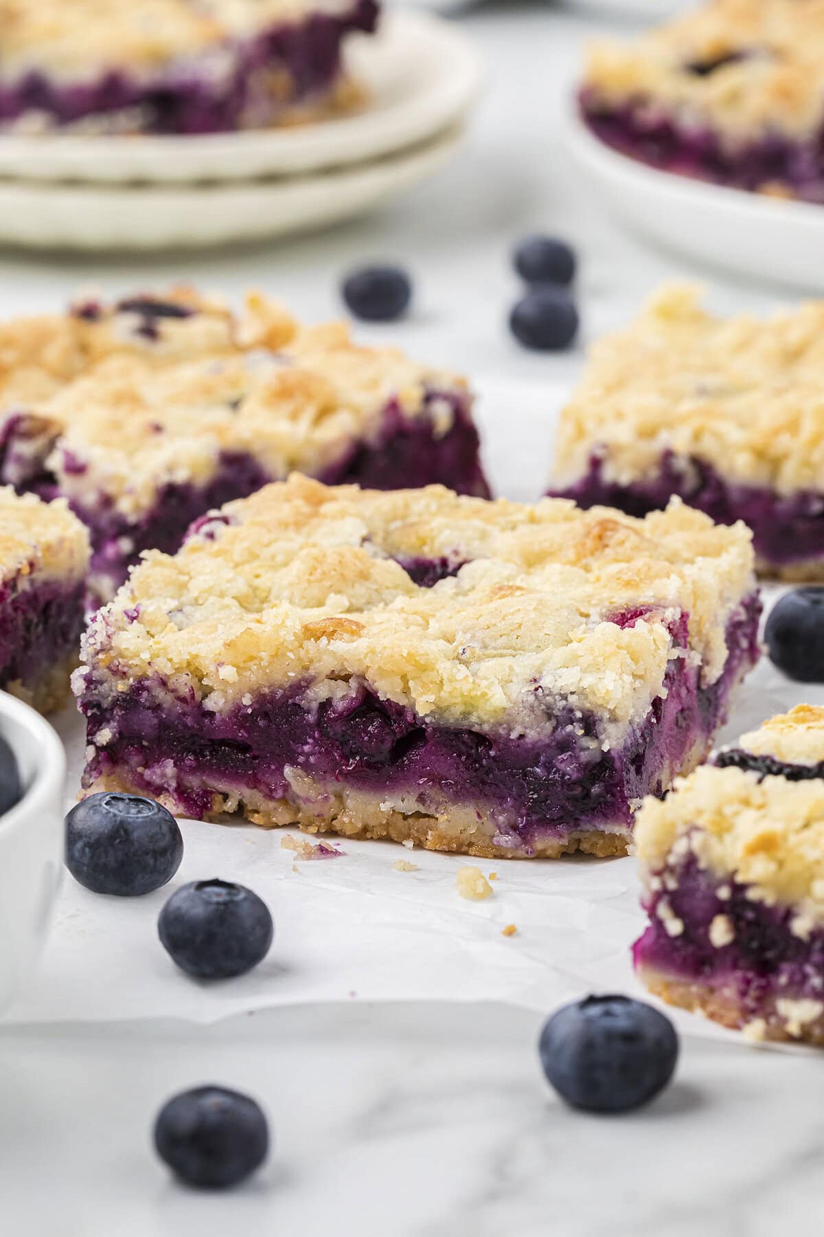 Blueberry pie bars on counter surrounded by fresh blueberries.