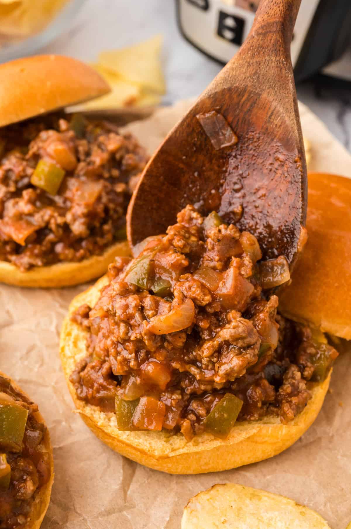 Wooden spoon spooning sloppy joe mixture onto bun.