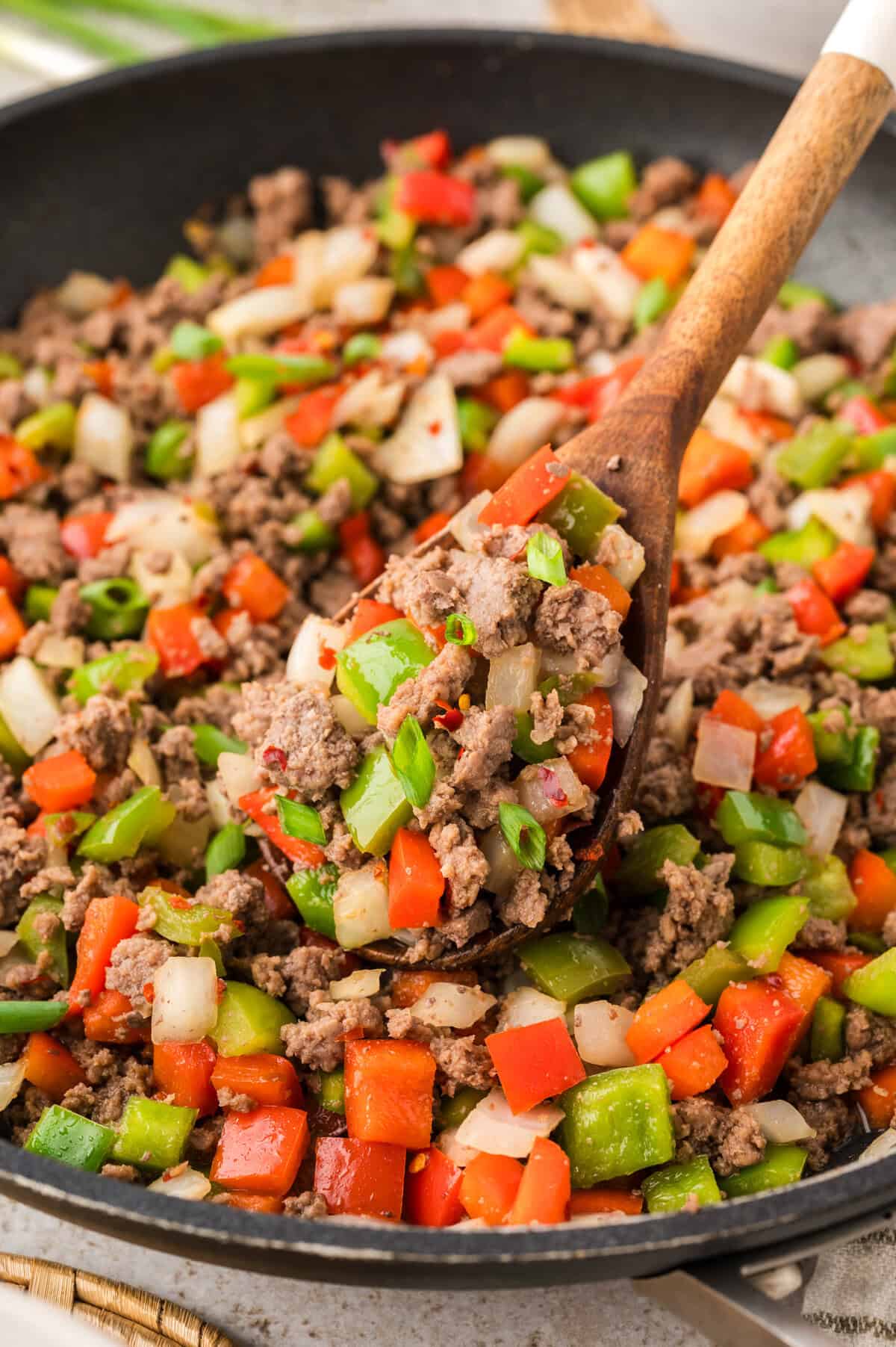 Wooden spoon full of beef and peppers.