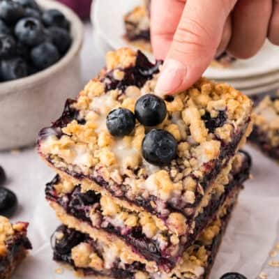 Hand grabbing a blueberry crumble bar off a stack.