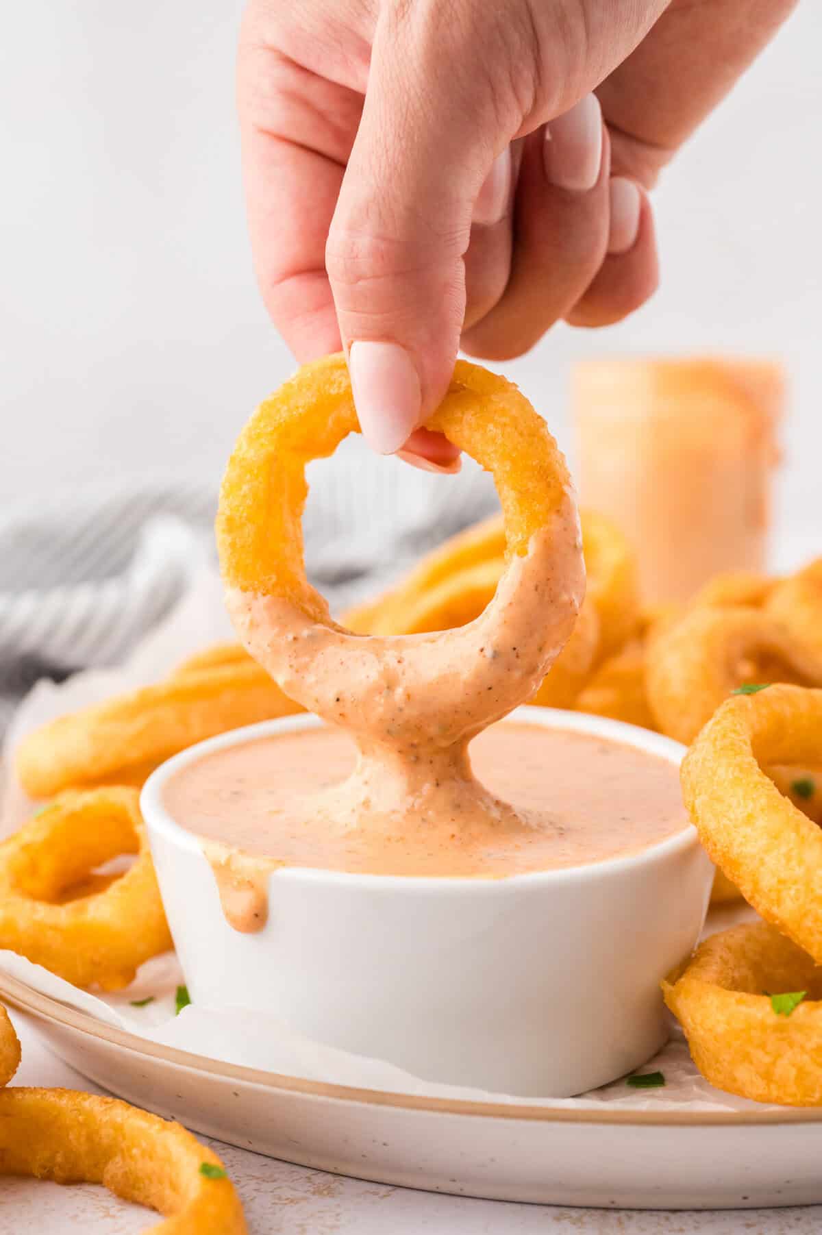 Hand dipping an onion ring into sauce.