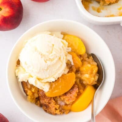 Bowl full of peach dump cake topped with ice cream.