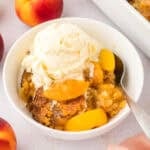 Bowl full of peach dump cake topped with vanilla ice cream.