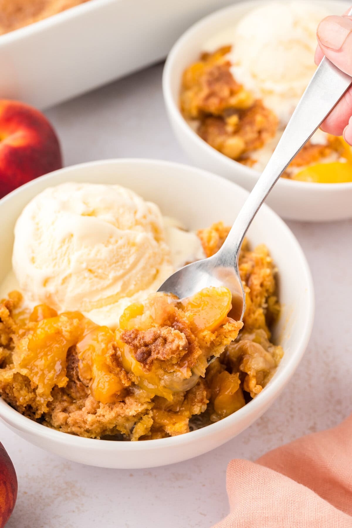 Bowl full of peach dump cake topped with ice cream.