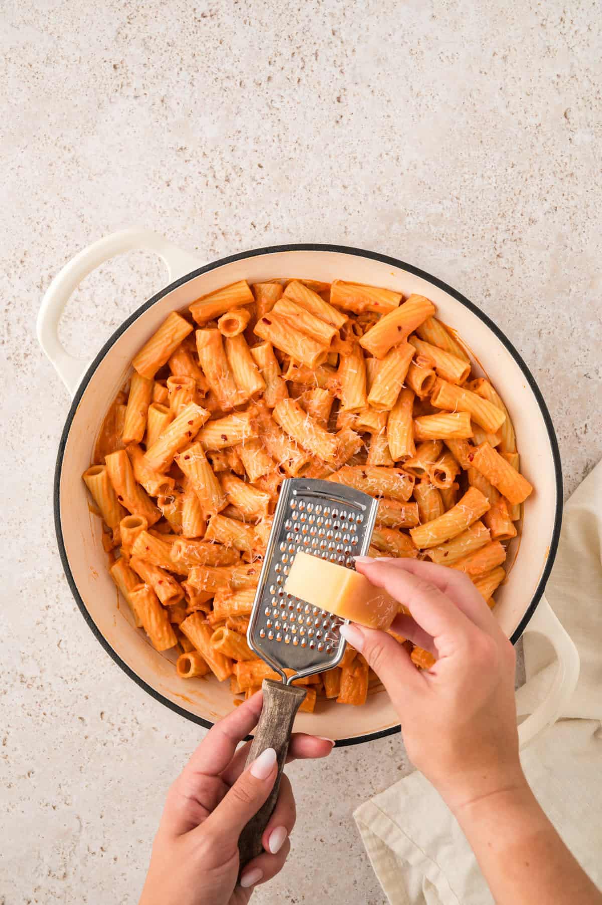 Parmesan being grated over spicy tomato rigatoni.