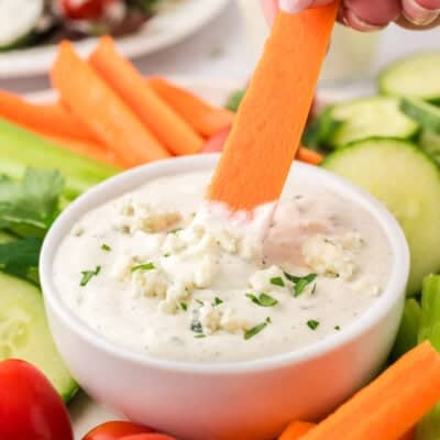 Carrot being dipped in blue cheese dressing.