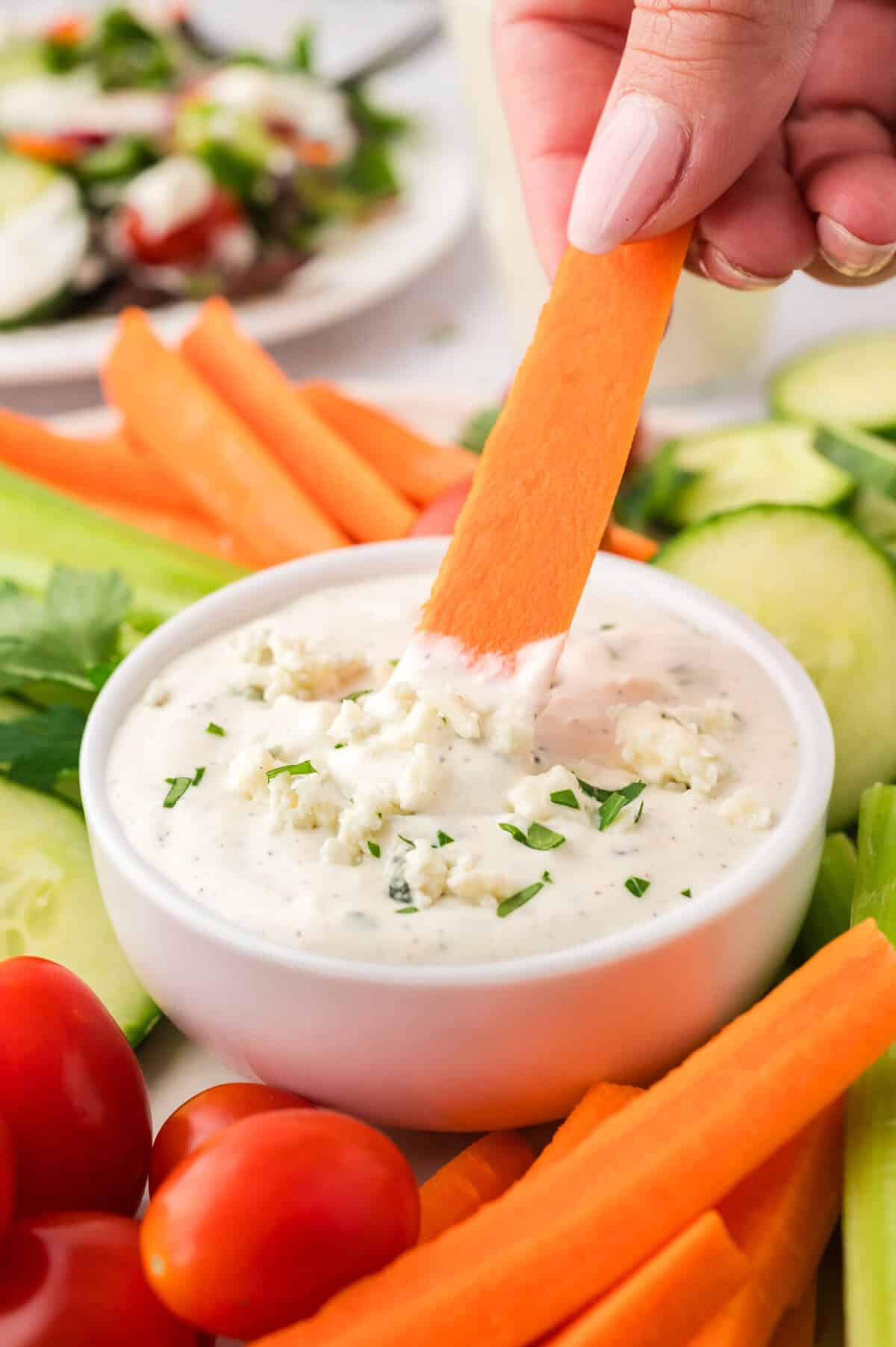 Carrot being dipped in blue cheese dressing.