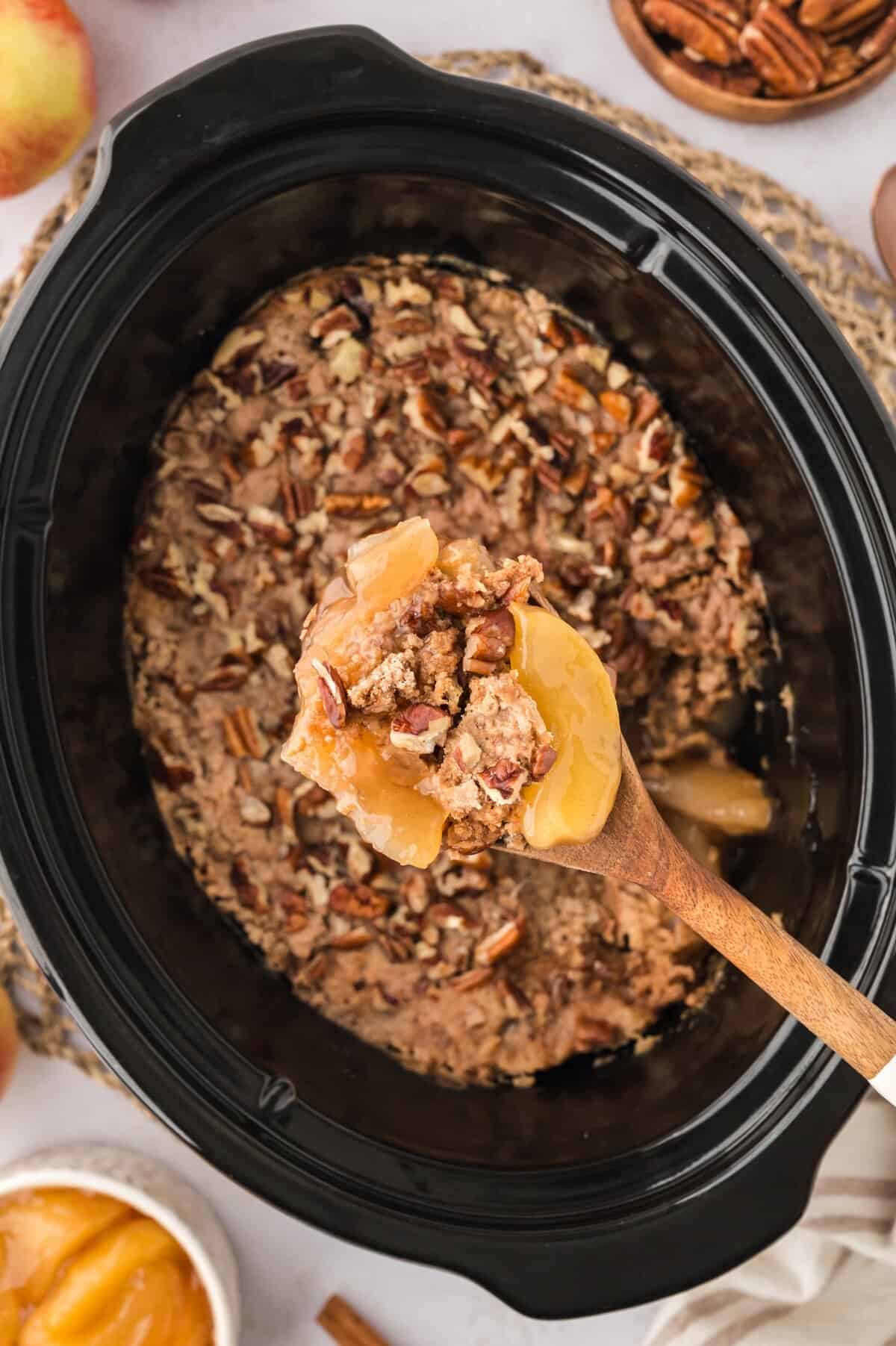 Spoon full of crockpot apple dump cake over black crockpot liner.