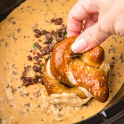 Pretzel being dipped in hot sausage beer cheese dip.