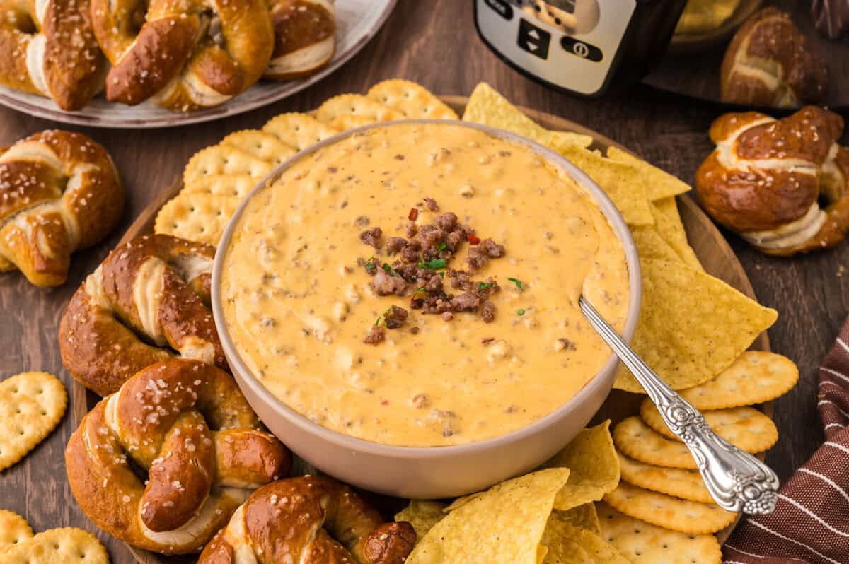 Crockpot beer cheese dip in small bowl surrounded by pretzels and chips.