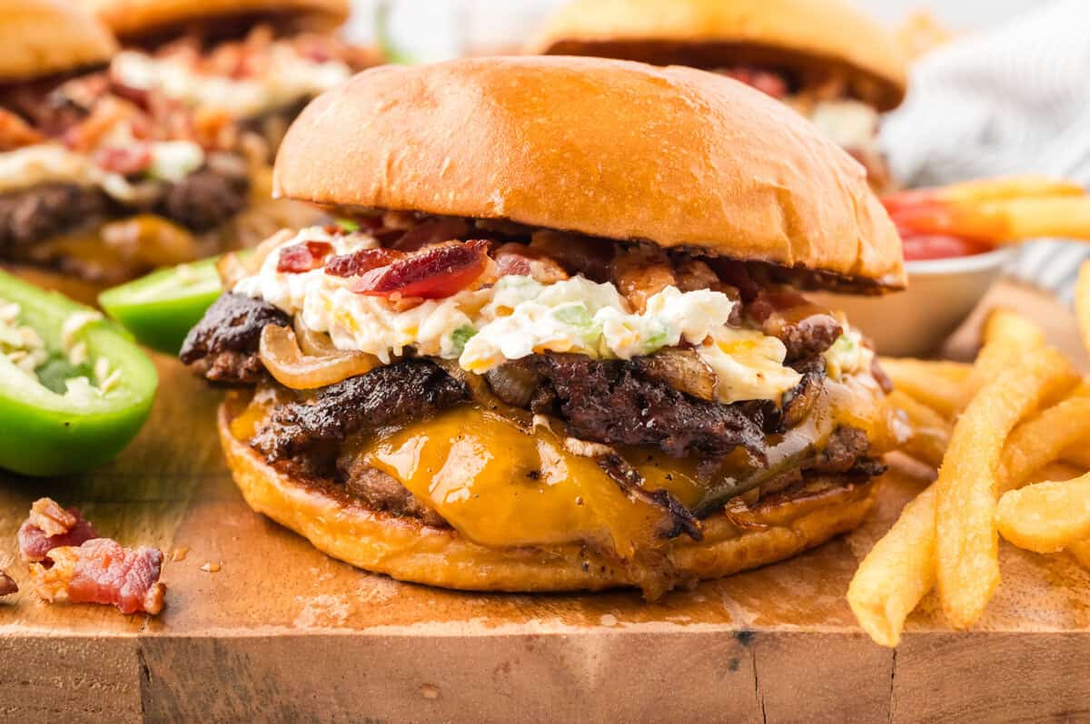 Jalapeno burger on bun on wooden cutting board with fries.