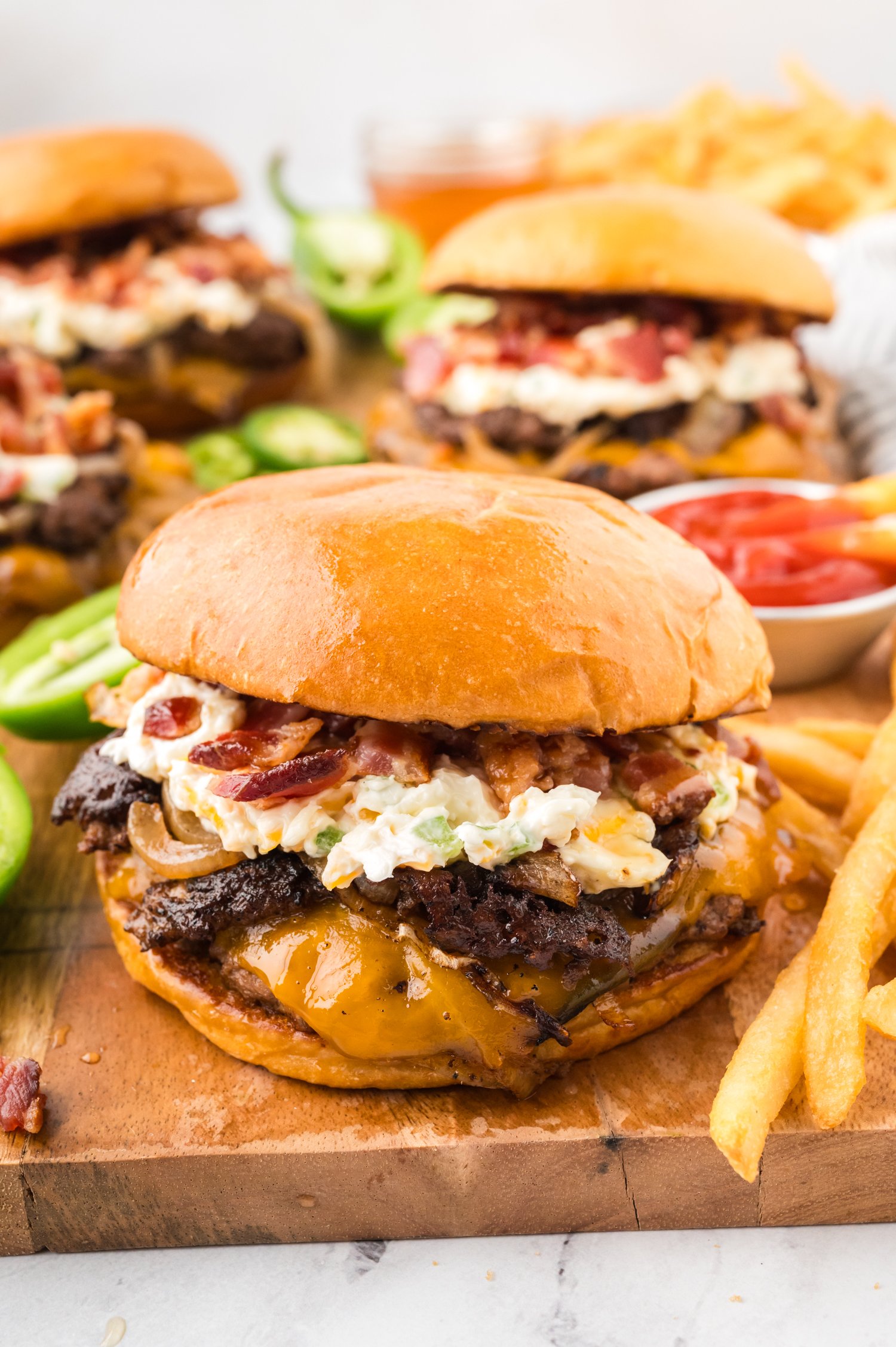 Jalapeno popper burger on wooden cutting board next to fries.