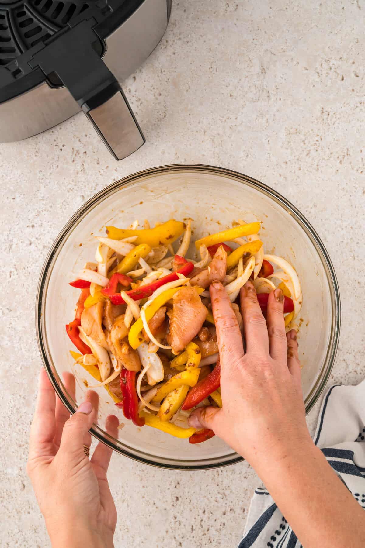 Chicken and fajita vegetables being seasoned in bowl.