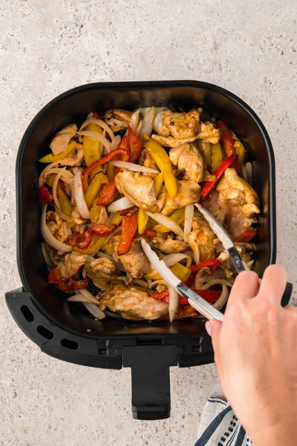 Chicken fajitas being stirred in air fryer basket.