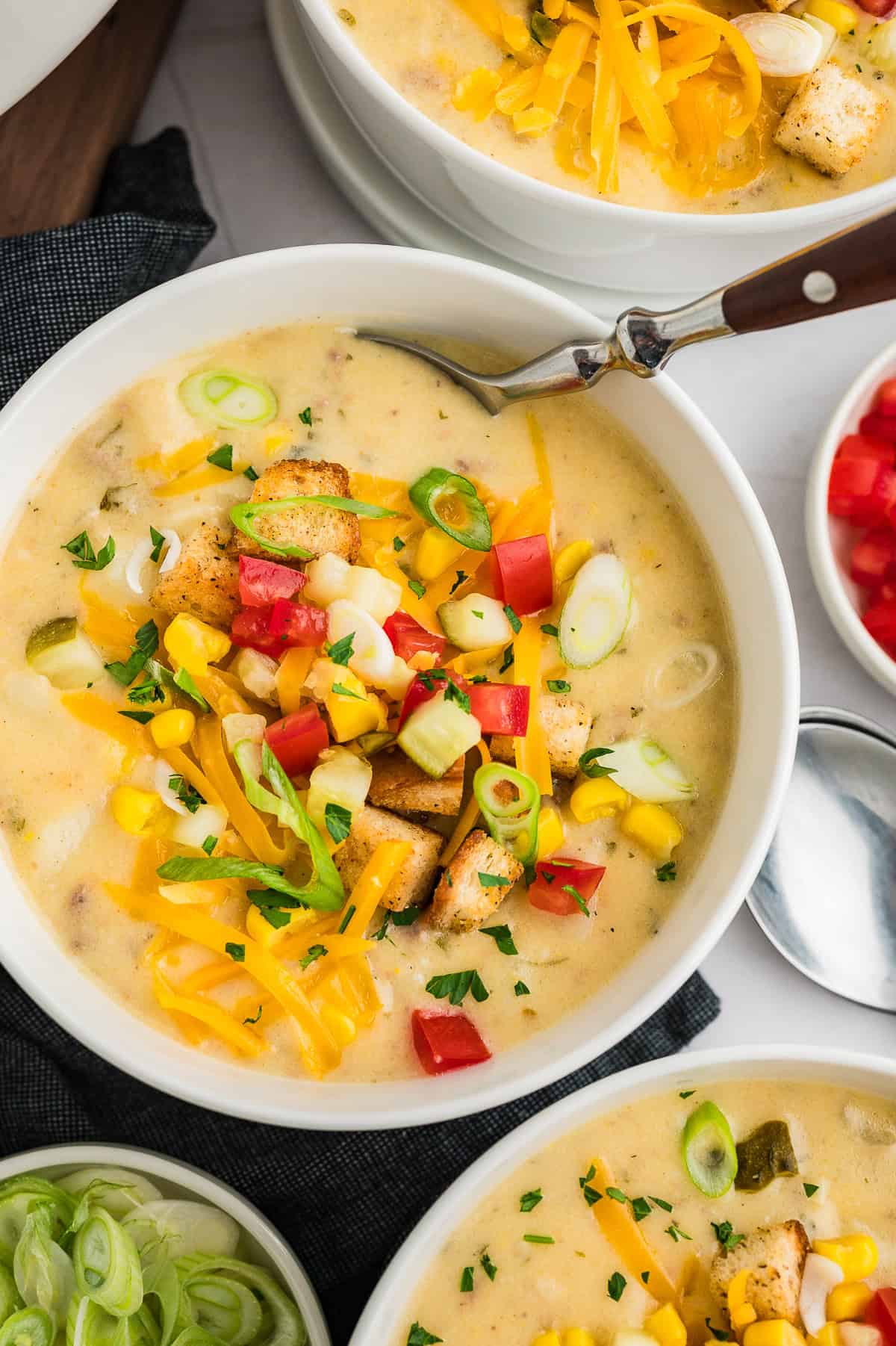 Bowl full of cheeseburger soup topped with tomatoes and pickles.