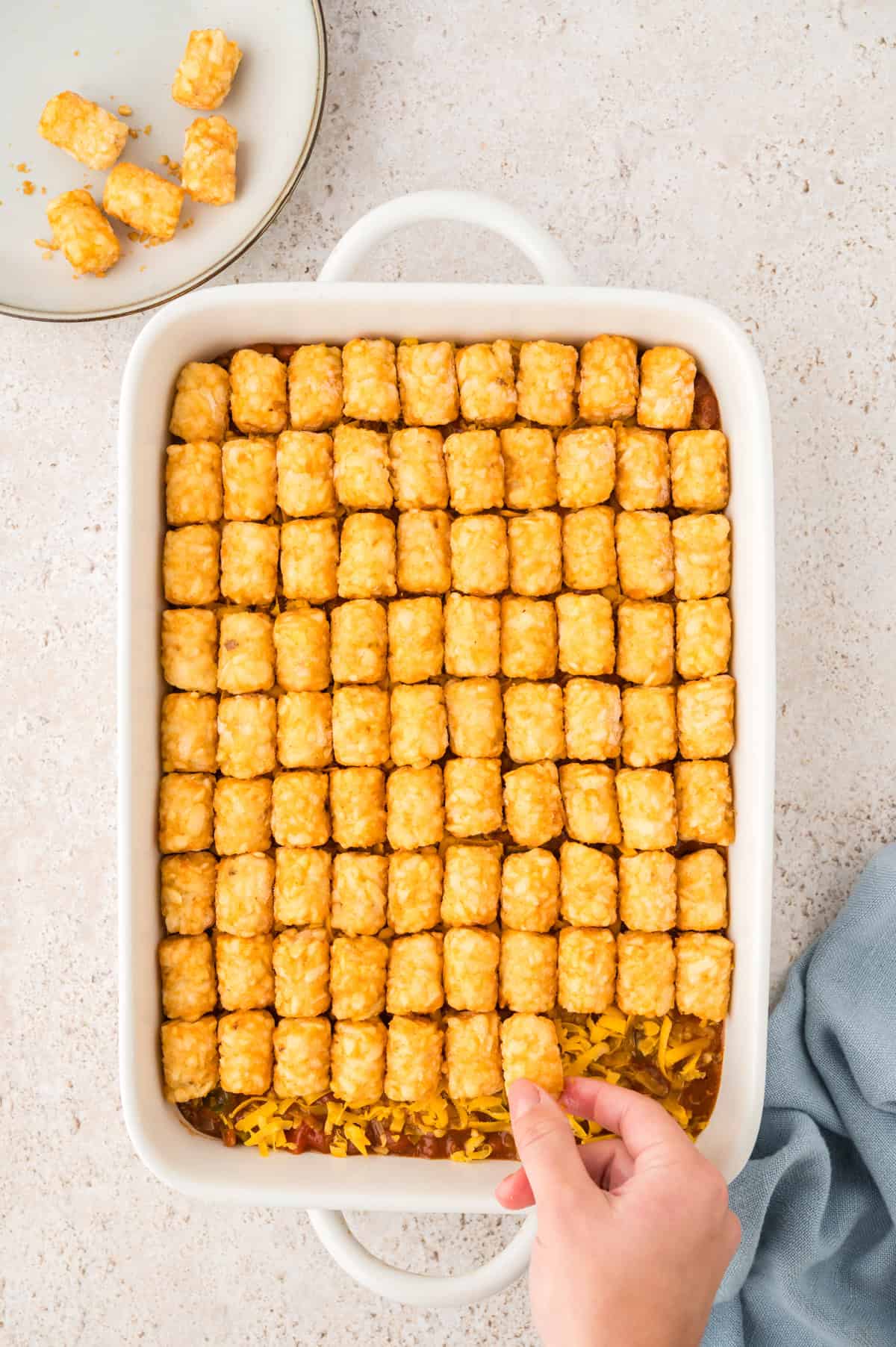 Tots being placed over chili in pan.