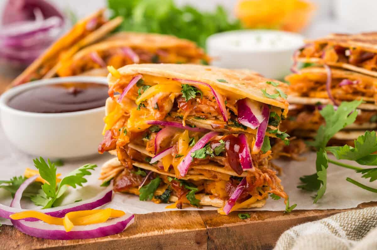 Stack of bbq chicken quesadilla wedges on wooden board.