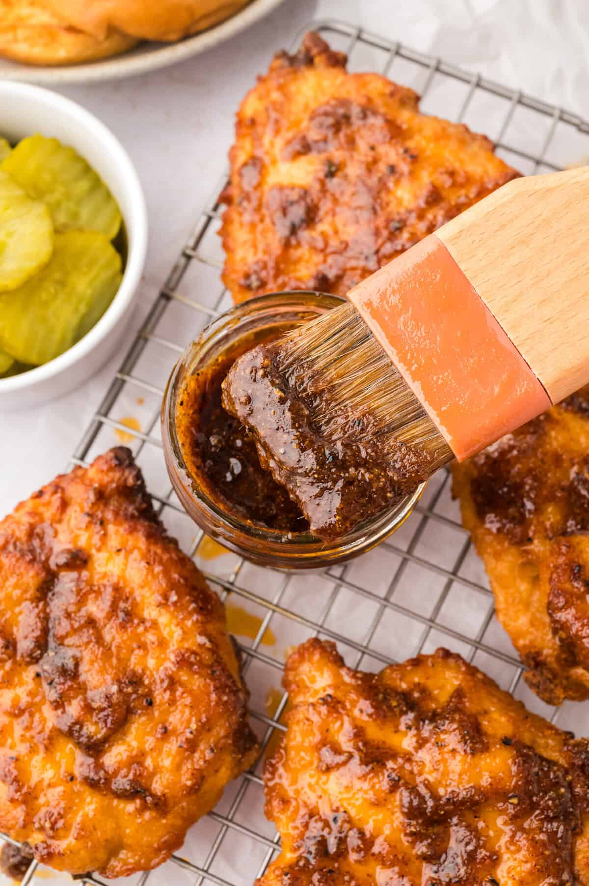 Nashville hot sauce in small jar being brushed over chicken.