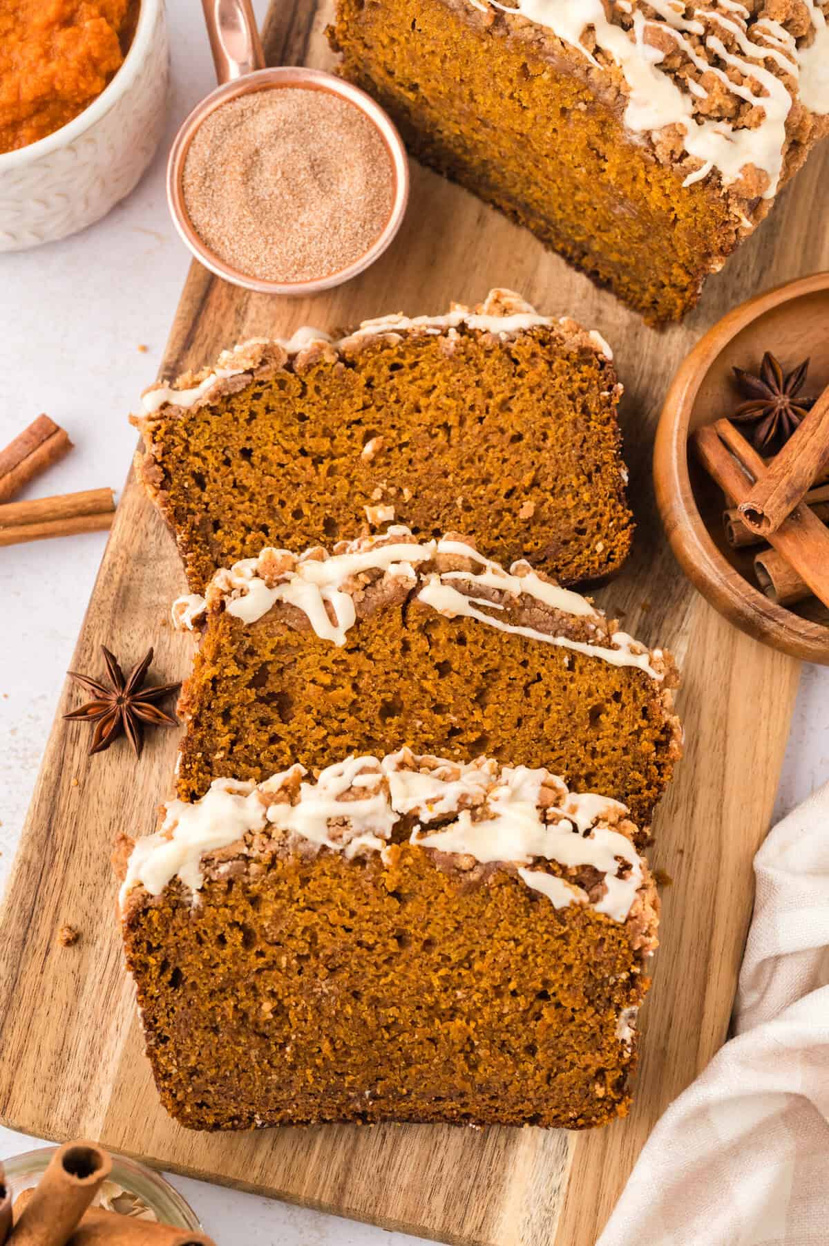 Slices of pumpkin bread with streusel topping and glaze on cutting board.