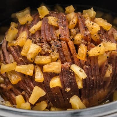 Spiral sliced ham coated in pineapples and brown sugar in crockpot.
