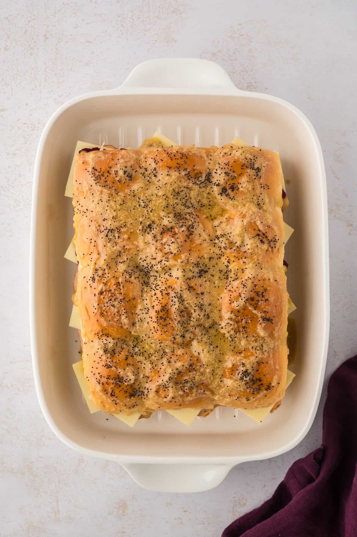 Sliders topped with buttery sauce in baking dish.