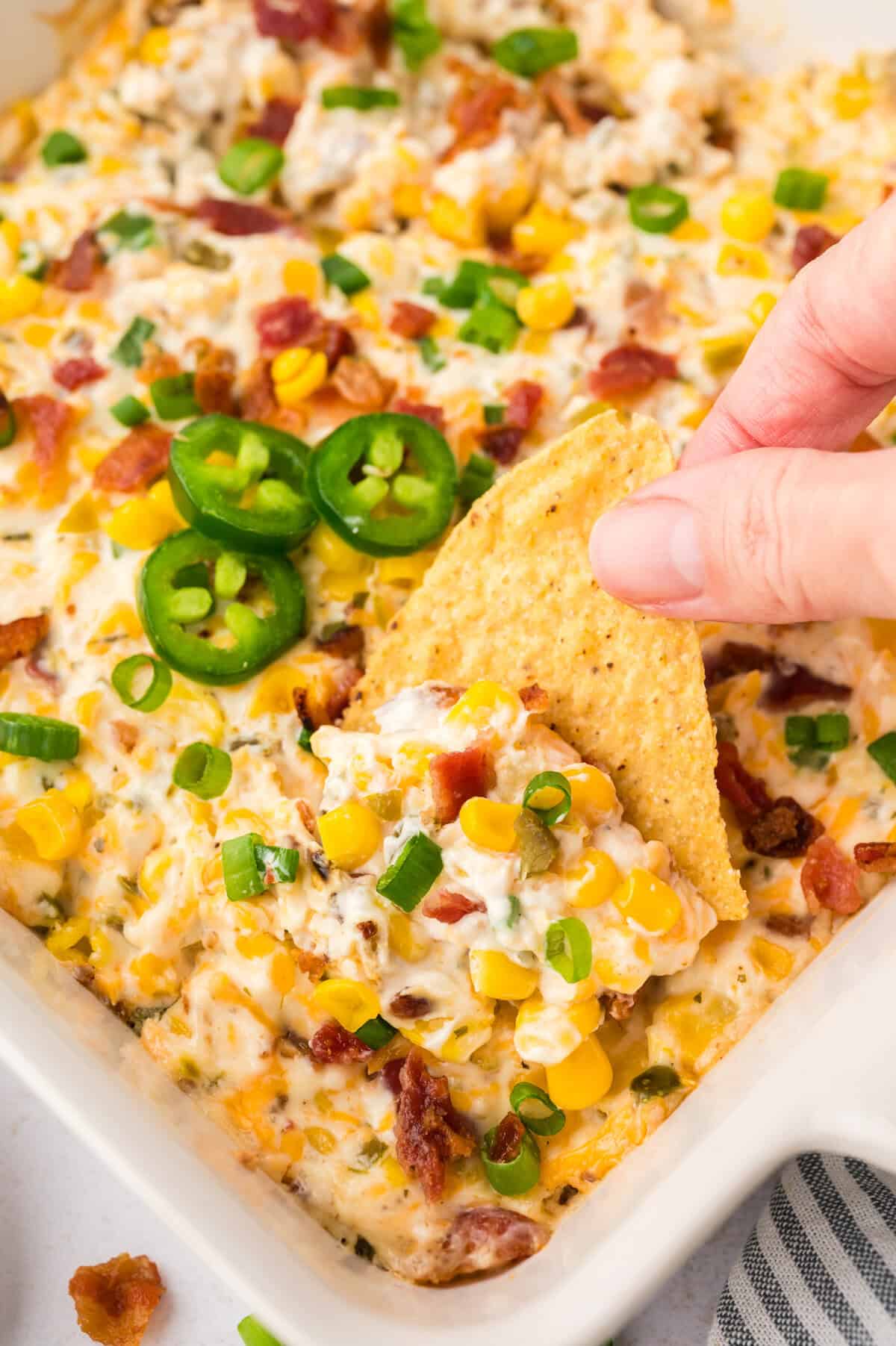 Hand dipping a chip into cream cheese corn dip.