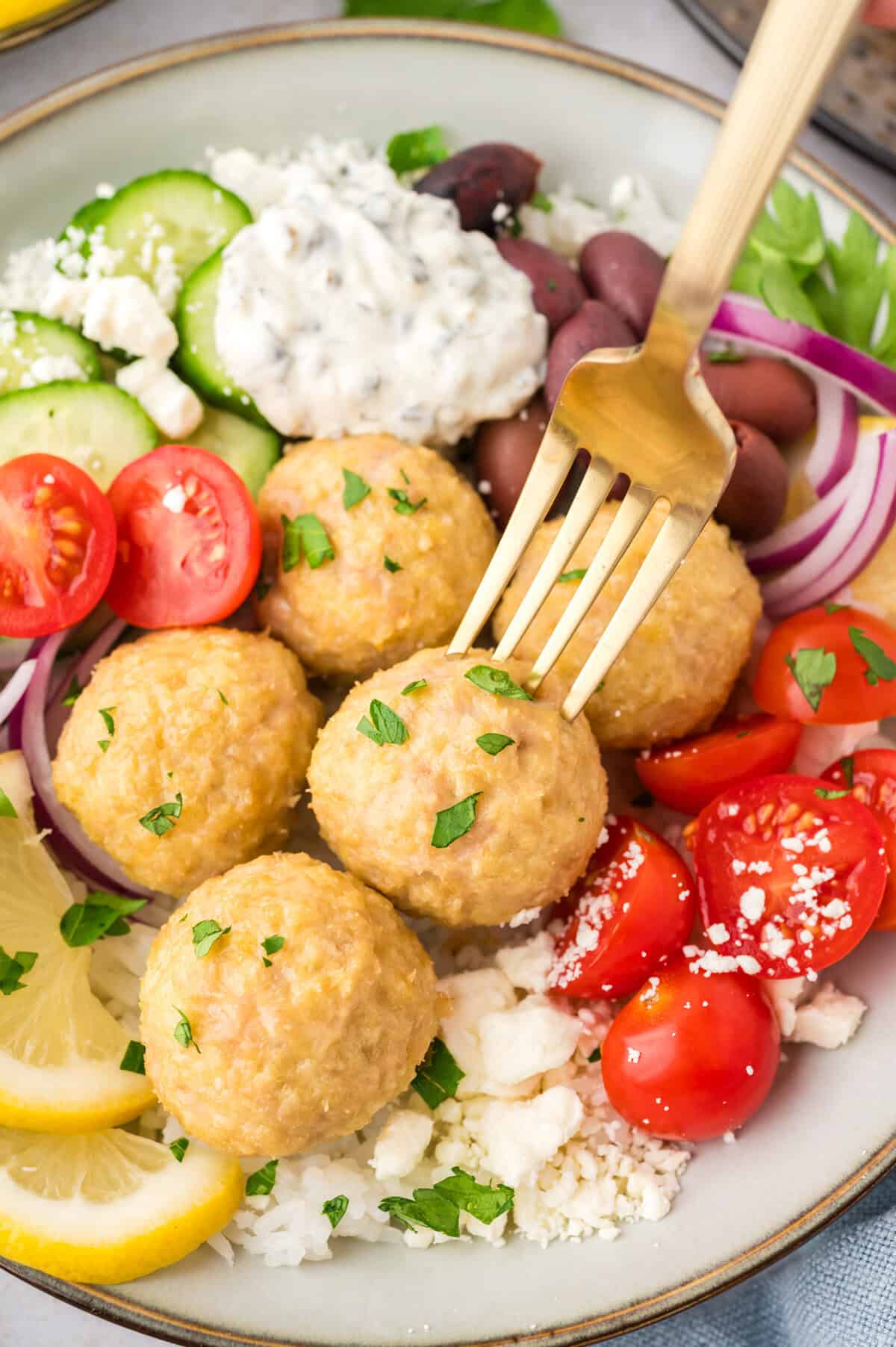 Baked chicken meatballs in a bowl with rice, tomatoes, and tzatziki.