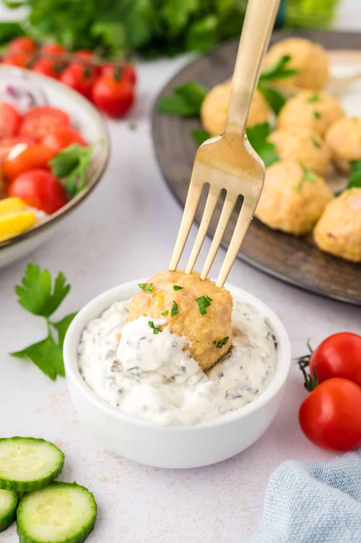 Baked chicken meatball on a fork being dipped in tzatziki sauce.