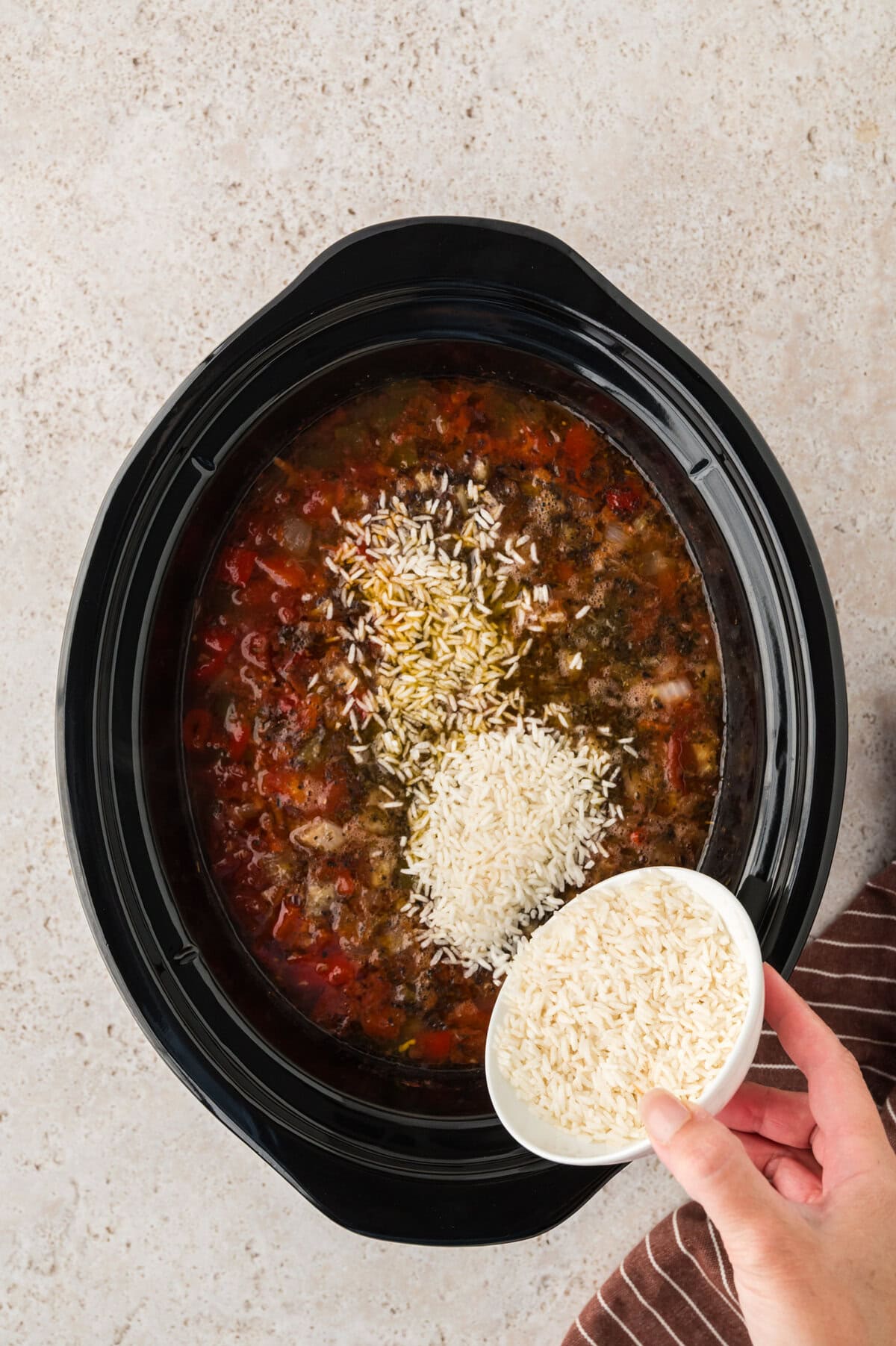 Rice being added to crockpot stuffed pepper soup.