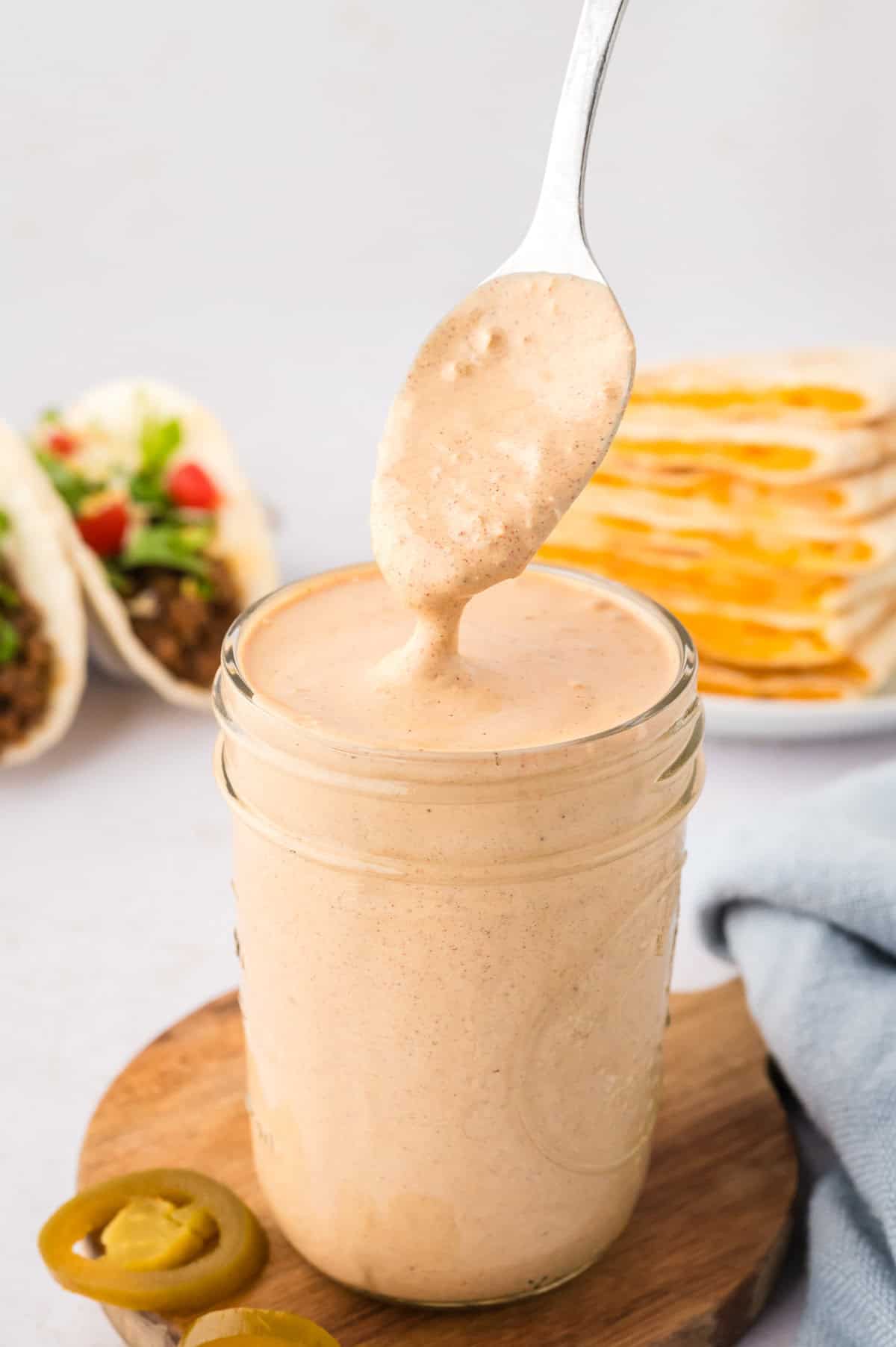 Creamy jalapeno sauce dripping off spoon into jar.