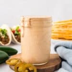 Jar of creamy jalapeno sauce in front of tacos and quesadillas.