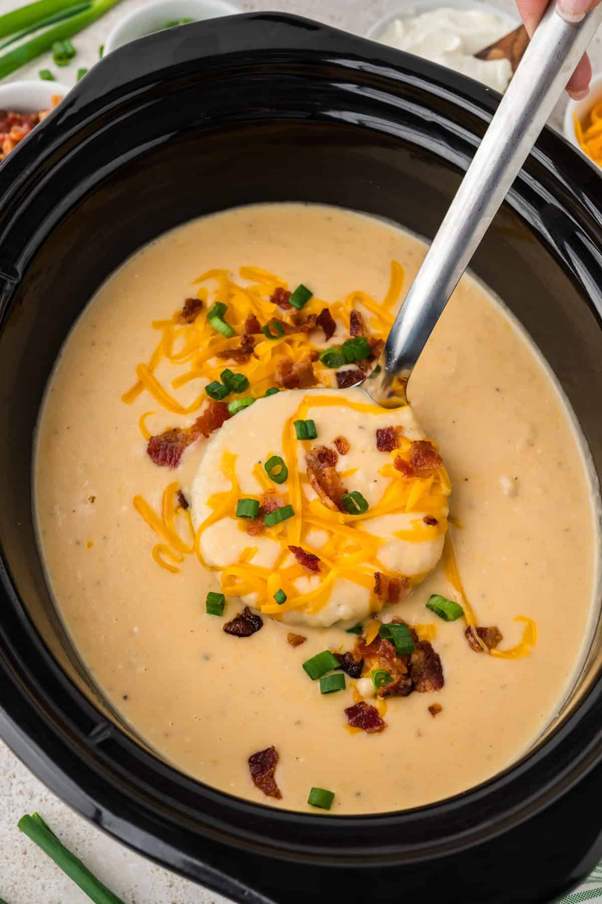 Crockpot potato soup made with hashbrowns on ladle over slow cooker.