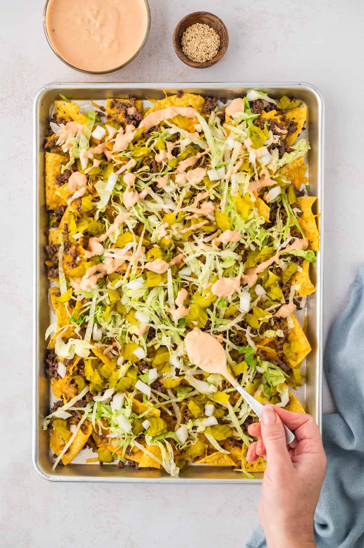 Homemade mac sauce being drizzled over Big Mac nachos.