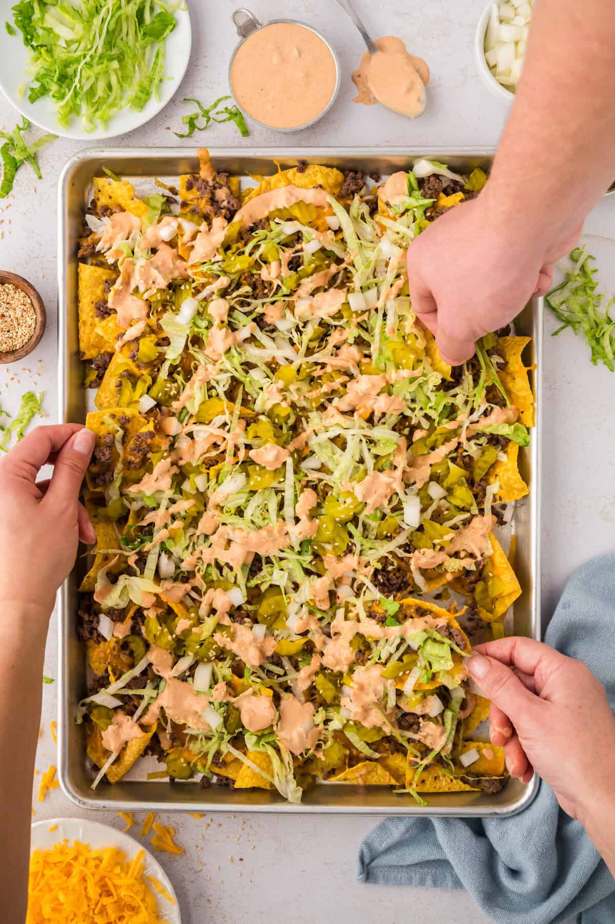 Hands grabbing chips off cookie sheet.