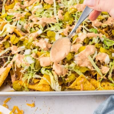 Spoon drizzling Big Mac sauce over nachos.