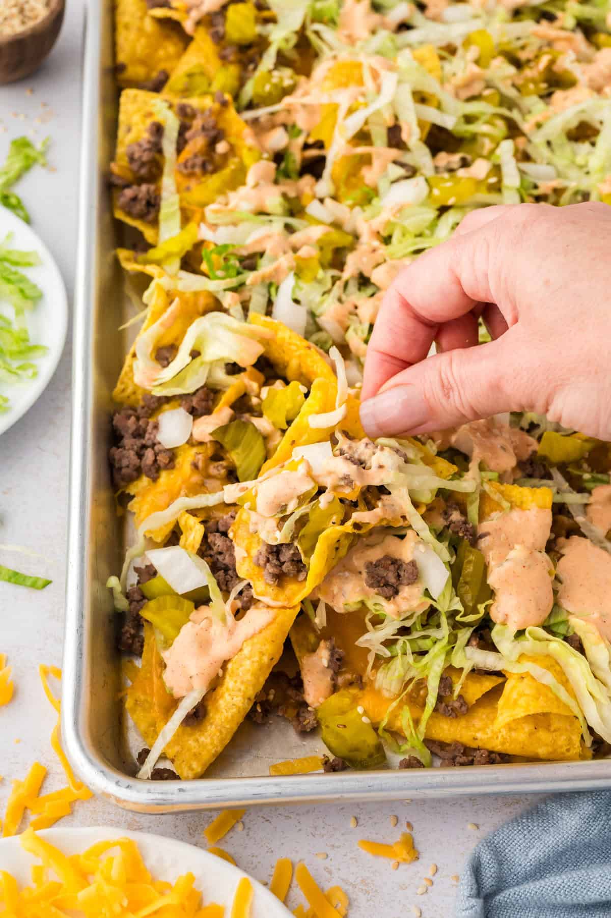 Hand grabbing a chip off a sheet pan topped with Big Mac nachos.