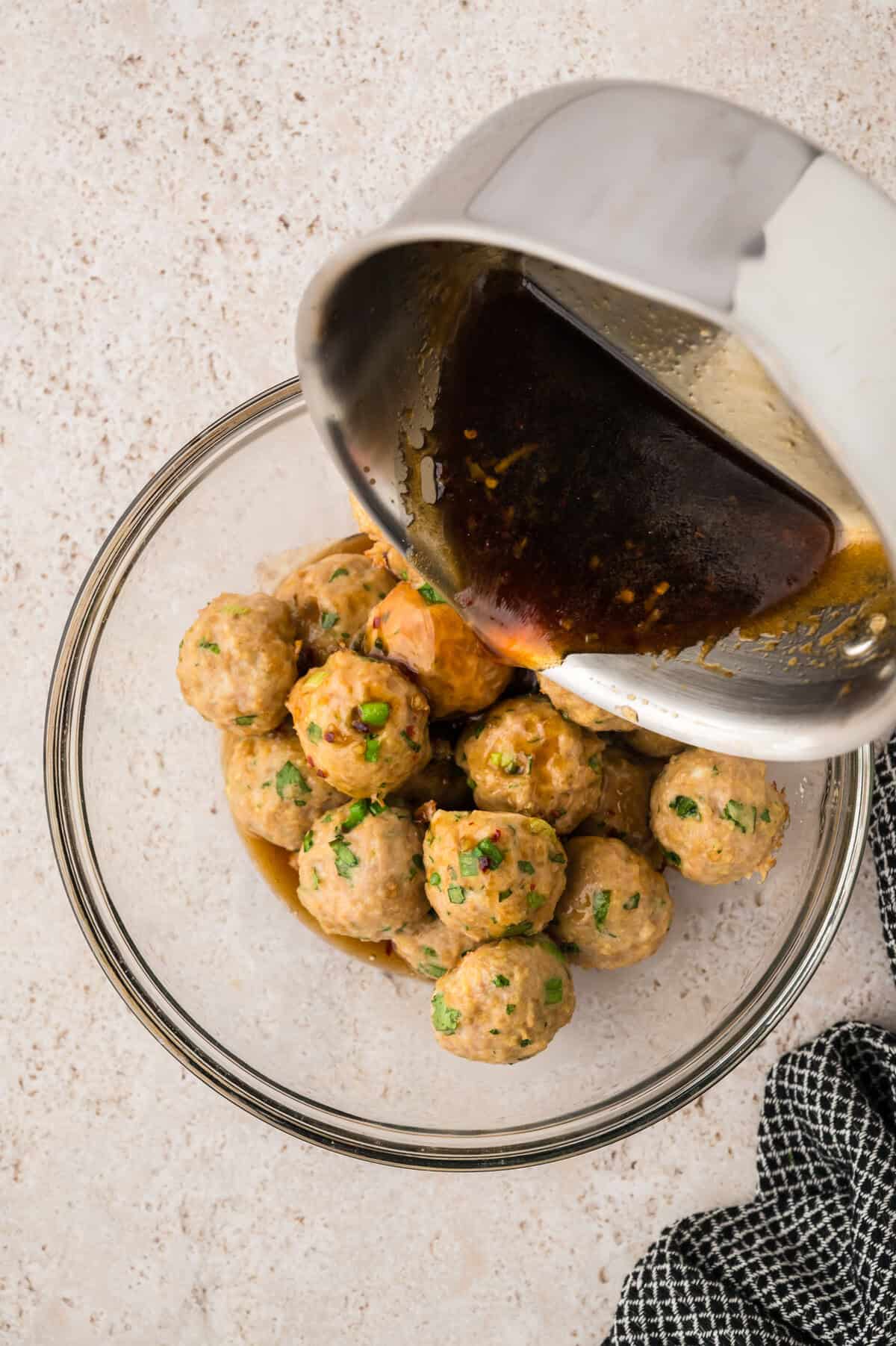 Sauce being poured over baked meatballs.