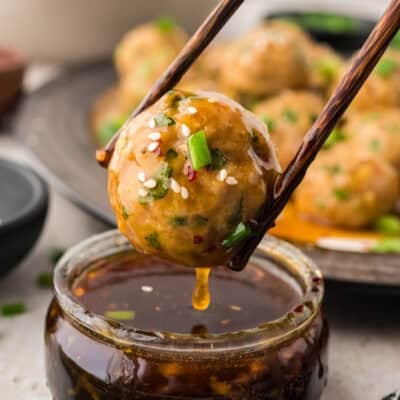 Asian chicken meatballs being dipped in sauce.