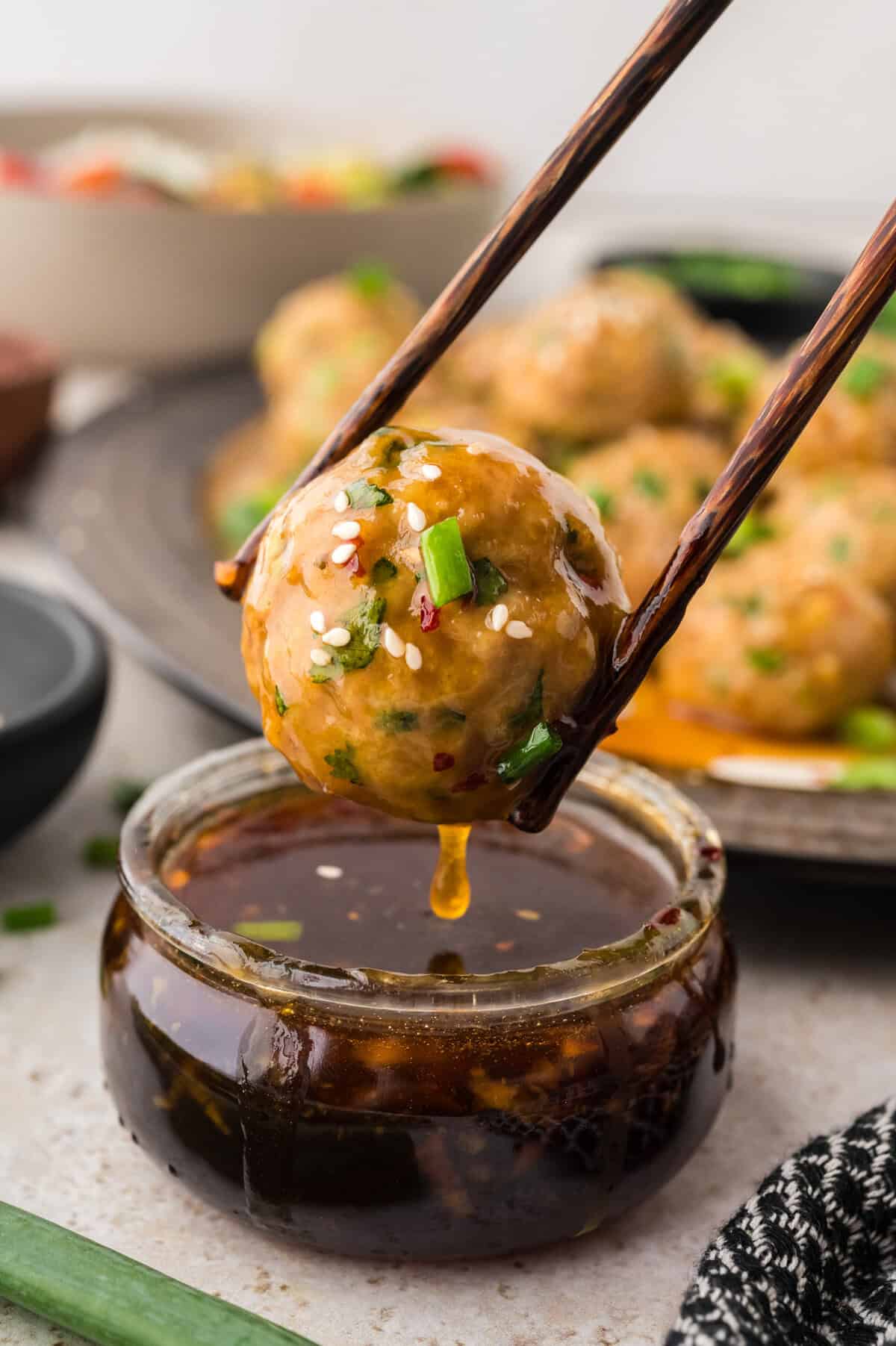 Asian chicken meatballs being dipped in sauce.