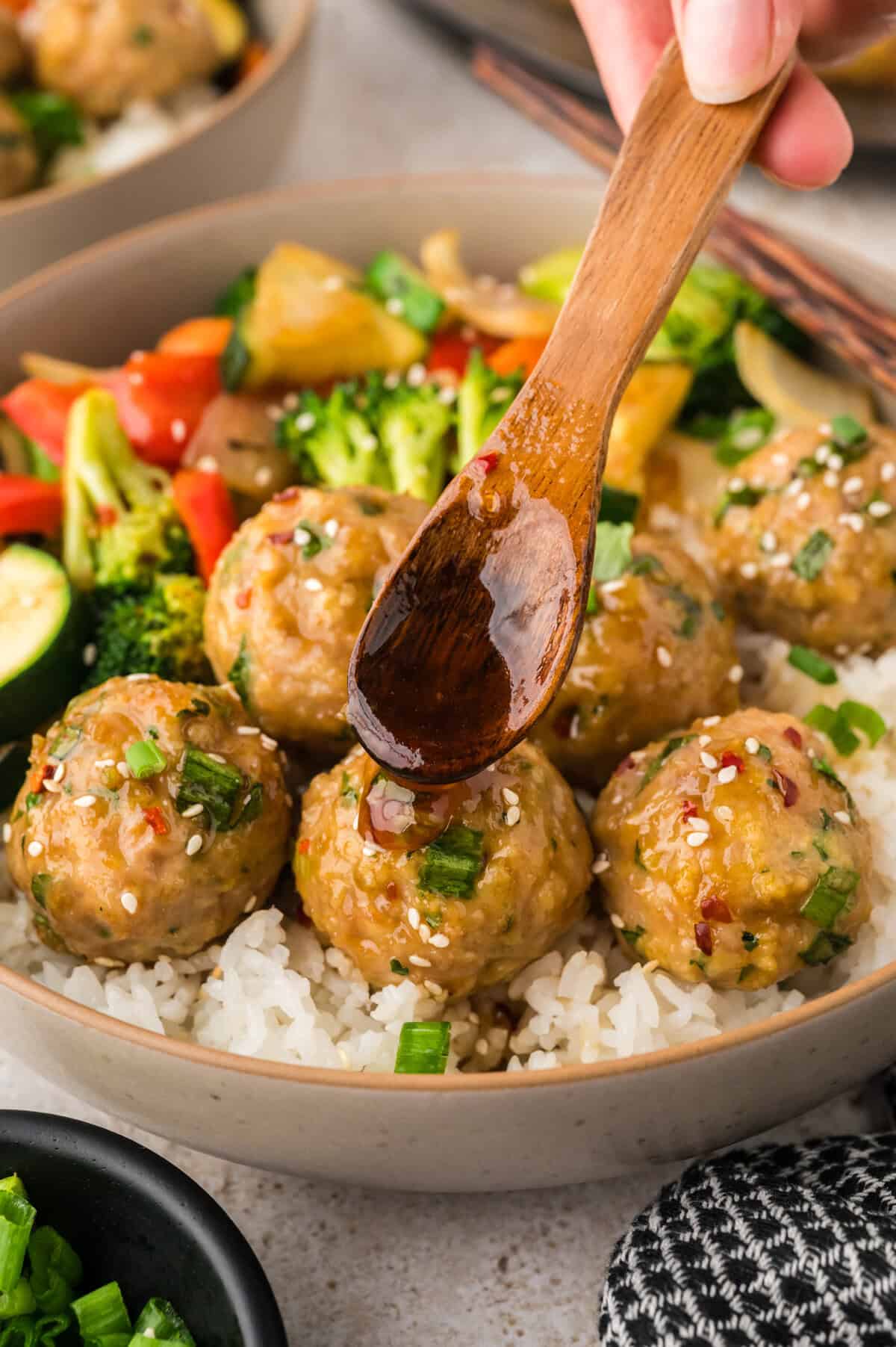 Sauce being drizzled over Asian chicken meatballs.